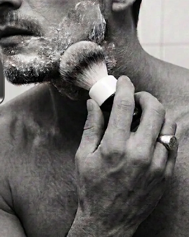 Fragment of a man shaving — jaw, brush and hand in hard monochrome light